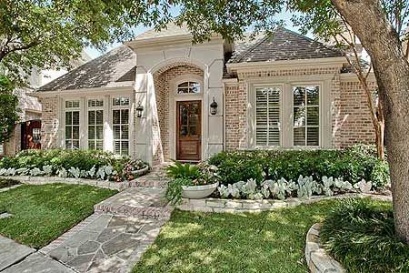 a house with landscaping in front of it and trees around the entrance to the home