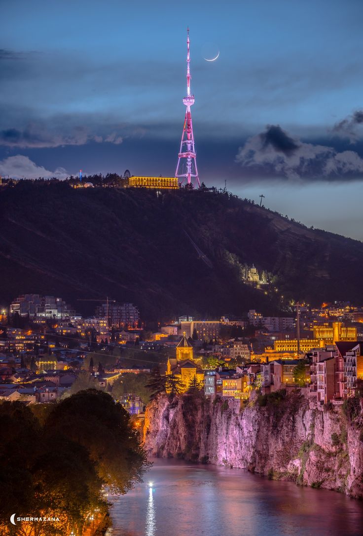 the city is lit up at night and it looks like it's on top of a hill