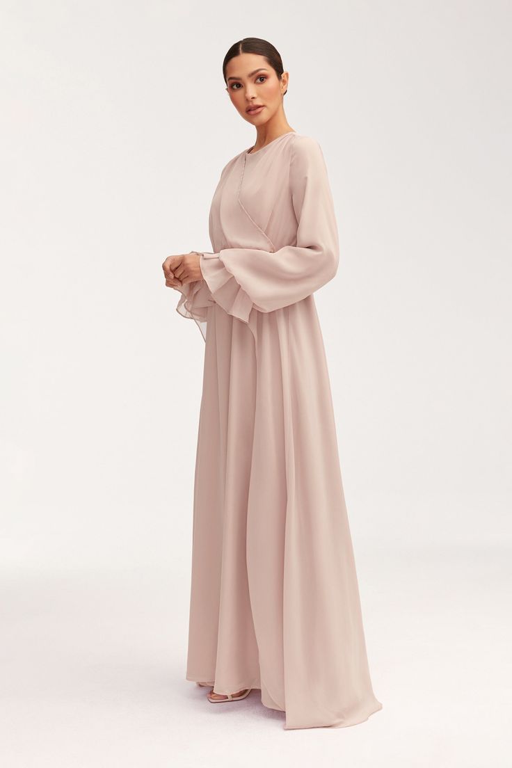 Introducing our Aara Chiffon Maxi Dress in Jasmine Pink. The flowy silhouette and balloon sleeves create an ethereal look, while the high low peplum design adds a touch of luxury. The overlay front panel adds texture and depth, making this dress a statement piece for any elegant occasion. Model is 5'7" and is wearing size XS/58". Grey Modest Outfit, Flowy Maxi Dresses, Chiffon Dress Hijab, Luxury Flowy Full-length Maxi Dress, Simple Soiree Dresses Hijab, Modest Graduation Outfit Hijab, Elegant Flowy Spring Abaya, Luxury Flowy Pink Maxi Dress, Simple Soiree Dresses