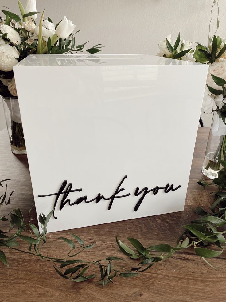 a thank you card sitting on top of a table next to flowers and greenery