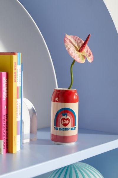 a red and white can with a flower in it on a shelf next to books