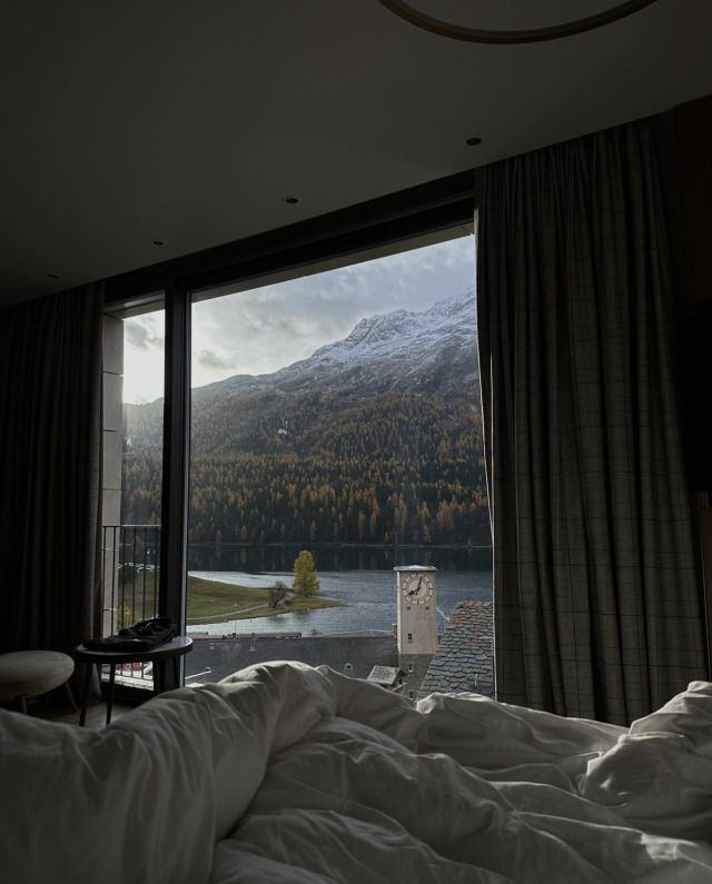 an unmade bed in front of a large window overlooking a mountain lake and forest