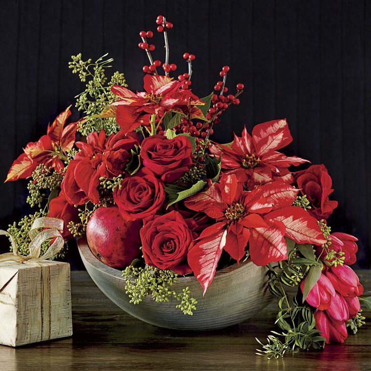 a bowl filled with poinsettia and red flowers next to a present box