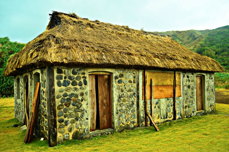 an old stone building with a thatched roof and door is in the middle of a grassy field