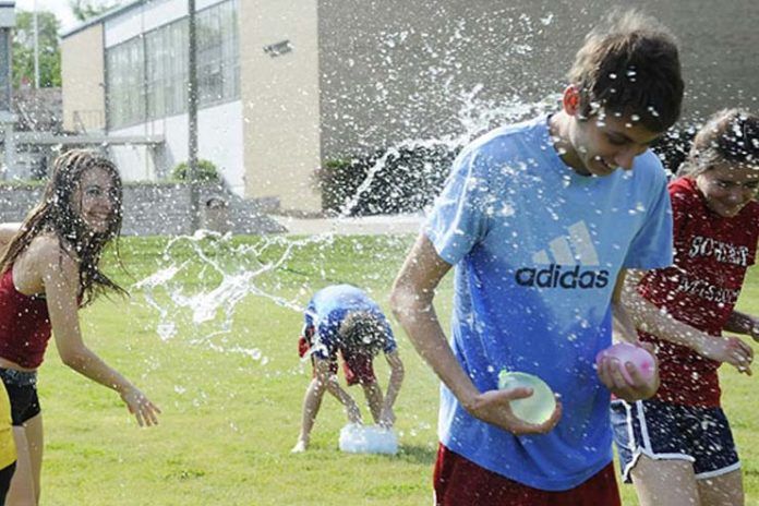 children playing in the sprinkles from a water fountain on a school field