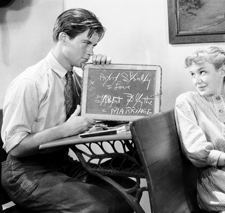 a man and woman sitting next to each other in front of a chalkboard sign