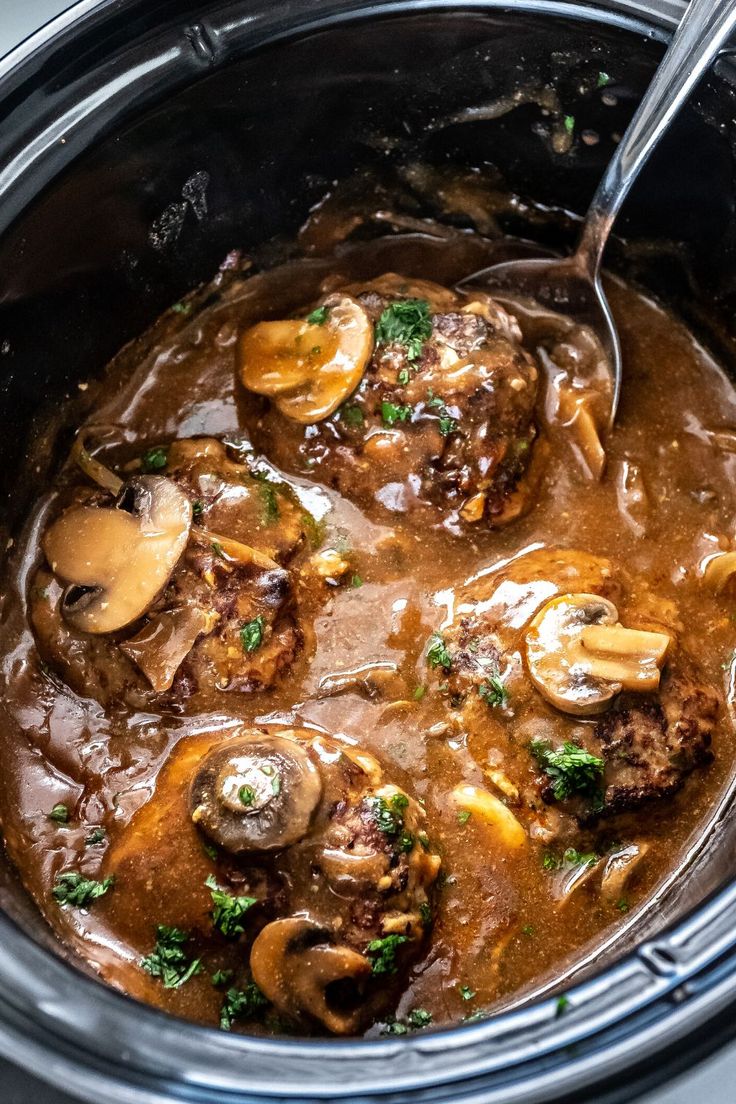 a slow cooker filled with meat and mushrooms