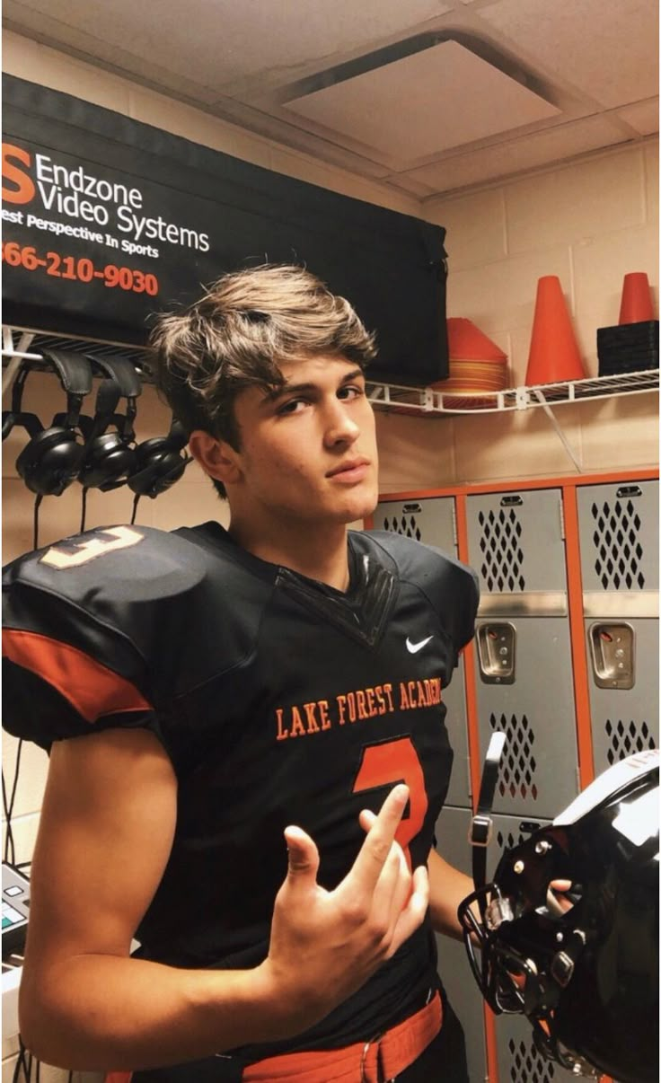 a young man wearing a black and orange football uniform standing in front of lockers