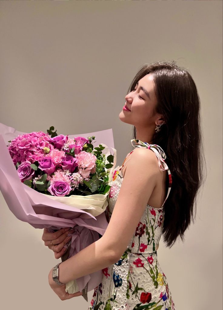 a woman holding a bunch of flowers in her hand and looking up at the sky