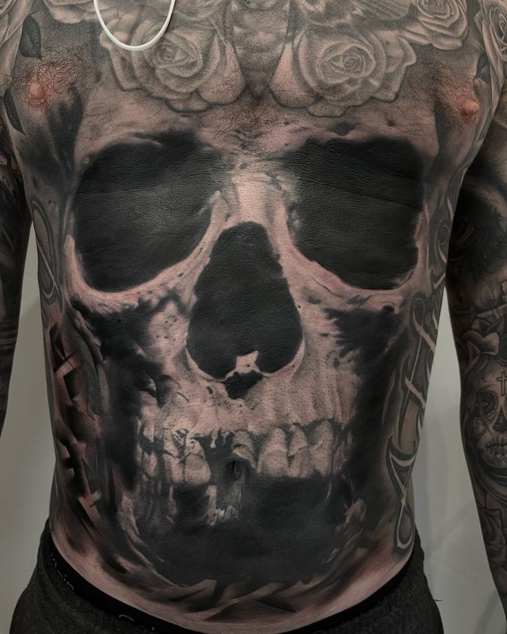 a man with tattoos on his chest and back is wearing a black shirt that has roses in it