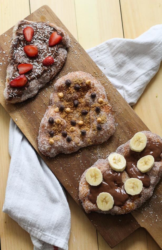 two heart shaped pastries on a cutting board with chocolate, bananas and powdered sugar