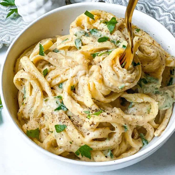 a white bowl filled with pasta and topped with parsley