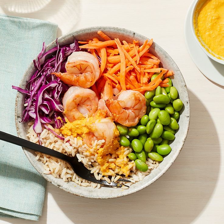 a bowl filled with rice, carrots, peas and shrimp next to a spoon