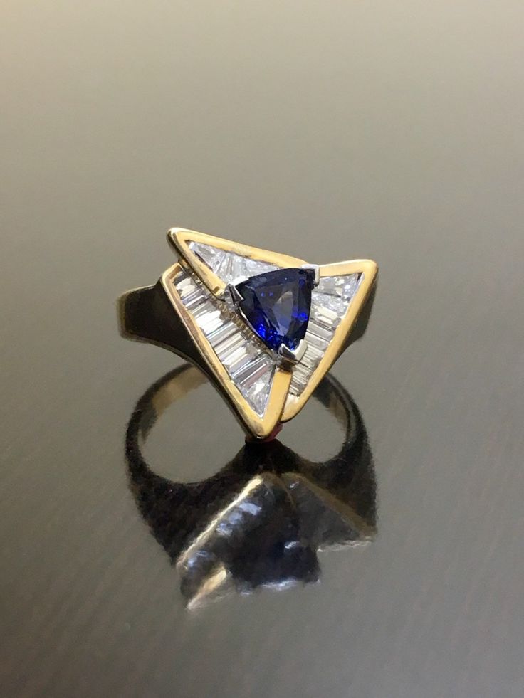 DeKara Designs Clearance Metal- 14K Yellow Gold, .583. 15.6 Grams. Stones- 1 Trillion Cut Ceylon Blue Sapphire 0.85 Carats, 21 Tapered Baguette Diamonds G-H Color VS2 Clarity 0.90 Carats. Size- Ring is a 6. FREE SIZING Art Deco Inspired Handmade 14K Yellow Gold Ceylon Blue Sapphire Diamond Ring. This ring is inspired by the Art Deco era with unique Trillion Cut Ceylon Blue Sapphire that is set in between three V prongs. There are 21 professionally channel set tapered baguette diamonds surroundin Gia Certified Trillion Cut Formal Rings, Formal Gia Certified Trillion Cut Ring, Fine Jewelry Yellow Gold Trillion Cut Sapphire Ring, Trillion Cut Yellow Gold Sapphire Ring, Trillion Cut Sapphire Ring In 14k Yellow Gold, Gia Certified Blue Art Deco Jewelry, Gia Certified Gold Sapphire Ring, Blue Art Deco Jewelry Gia Certified, Blue Sapphire Ring With Trillion Cut Diamond