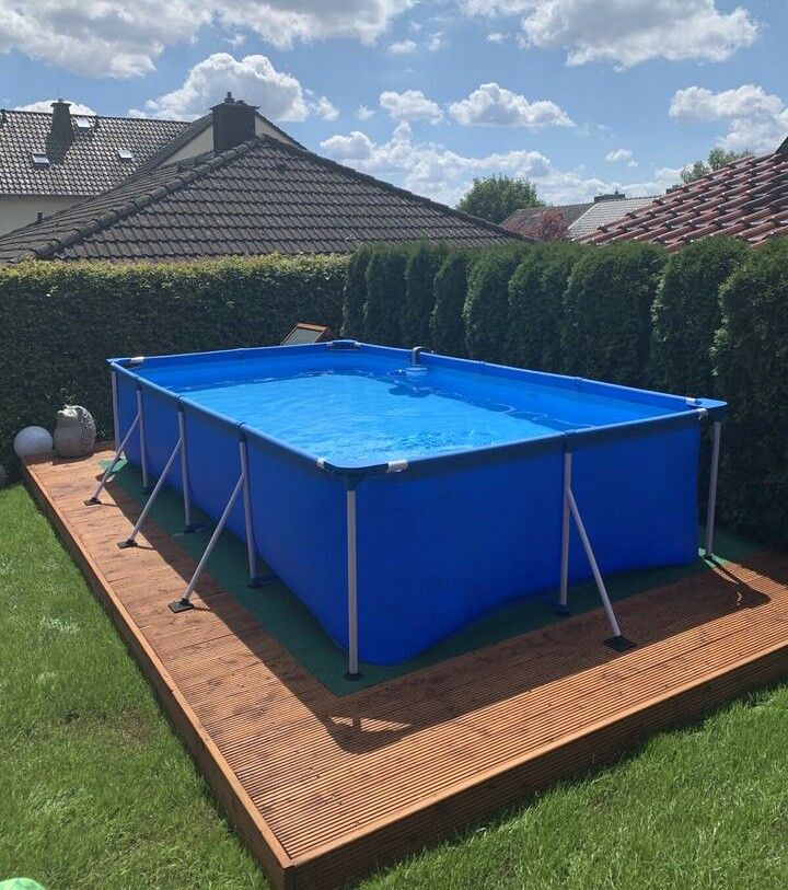 an above ground swimming pool on a deck in a backyard with green grass and bushes