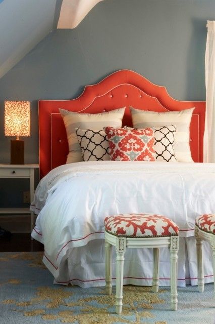 a bedroom with a red headboard and white bedding, two stools at the foot of the bed