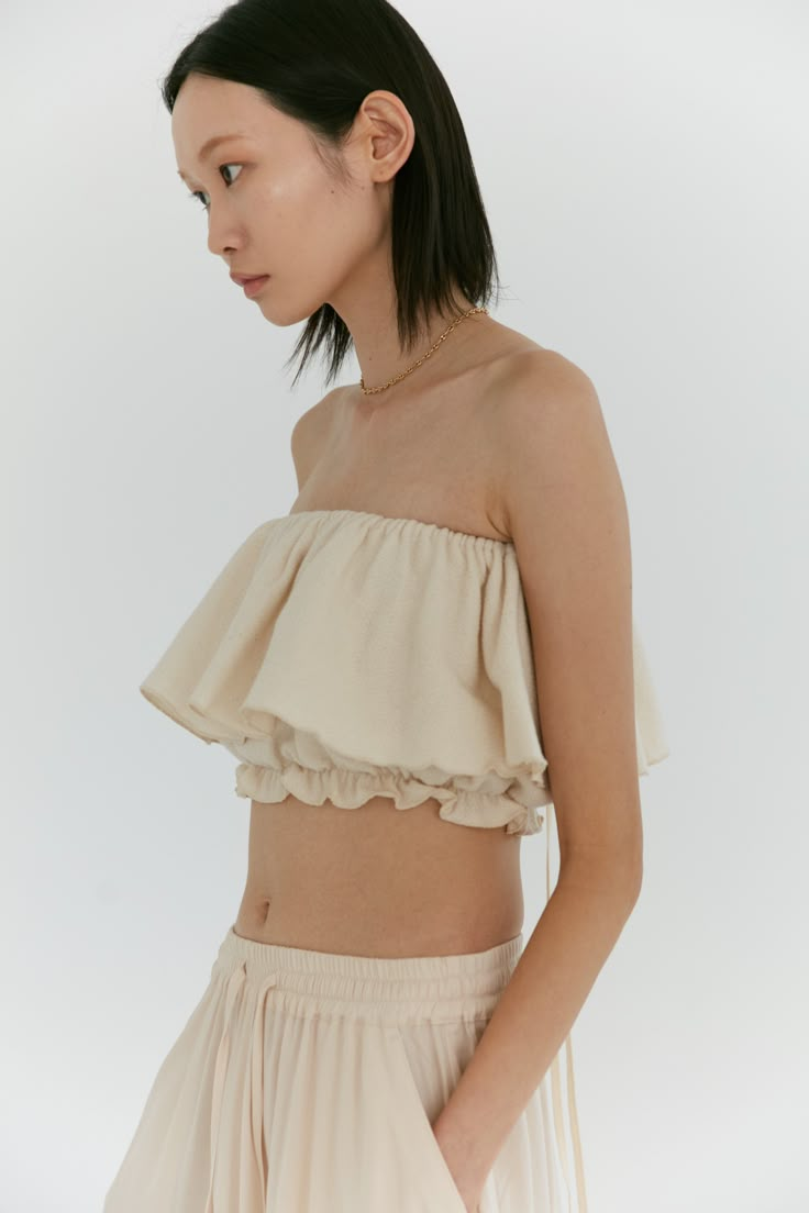 Our signature convertible ruffle top is so versatile, it can adjust to any mood. Manipulated into a countless number of ways, this elasticized top can be worn as a simple tube top, to off the shoulder or even as an asymmetric one shoulder. Choose to tie the long ties into a bow or over the shoulder into spaghetti straps or halter - the possibilities are endless. Made in our dandelion cotton - this fabric features a lightly brushed, textured exterior while maintaining a soft breathable interior. Cotton Ruffle Top, Neutral Loungewear, Diwali 2024, Slouch Socks, Pretty Blouses, Strapless Tops, Stylish Dress Designs, Ruffle Top, Fashion Essentials