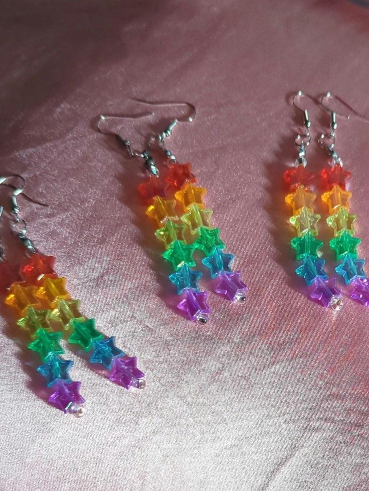 three pairs of earrings with multicolored beads on pink fabric background, closeup