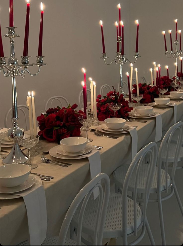 a long table with white plates and red roses on it is set for a formal dinner