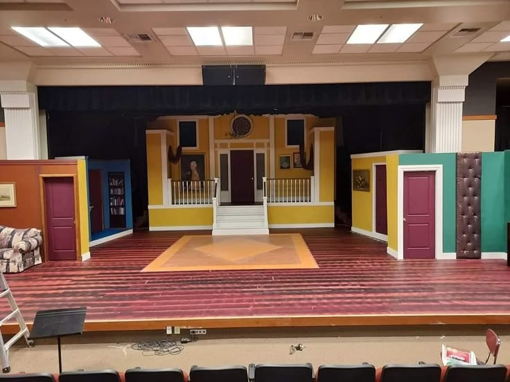 an empty stage with chairs and couches in front of the stage is painted bright colors