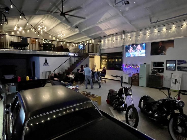 several motorcycles are parked in a garage with people standing around and watching television on the wall