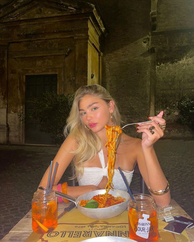 a woman sitting at a table with spaghetti in front of her face and holding a fork