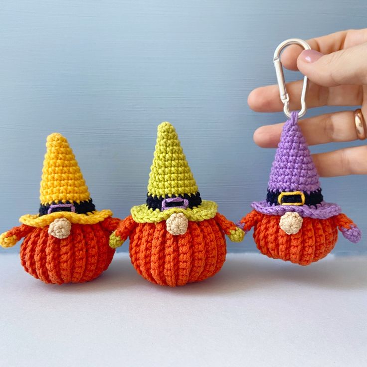 three crocheted pumpkins are being held by a person with a keychain