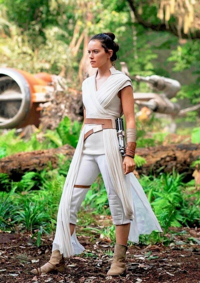 a woman in a white outfit standing on top of a dirt ground next to trees