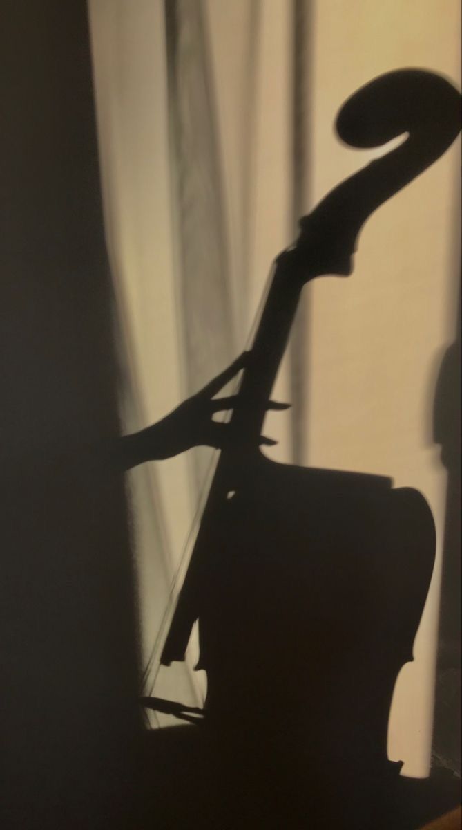 the shadow of a chair in front of a curtain with a guitar on it's back