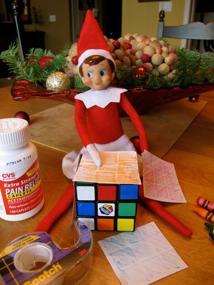 an elf sitting on top of a wooden table next to a rubix cube and glue