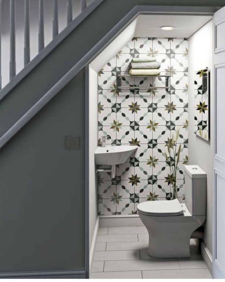 a white toilet sitting under a stair case next to a bathroom sink and toilet paper