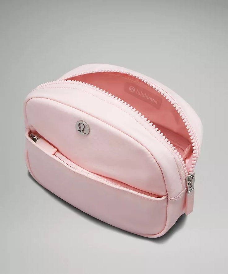 a pink cosmetic bag with zippers on the front and side, sitting on a gray surface