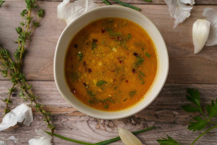 a white bowl filled with soup sitting on top of a wooden table next to flowers