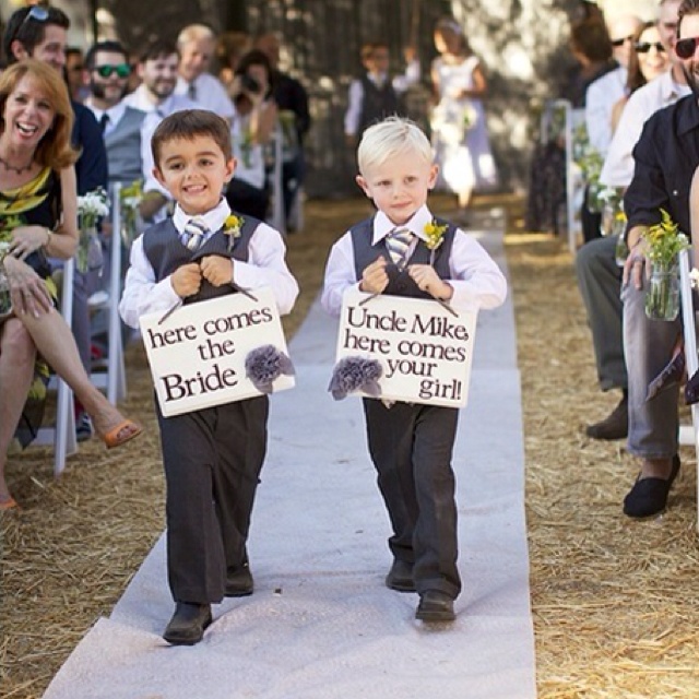 two young boys are walking down the aisle with signs on their laps that say, here comes the bride and groom