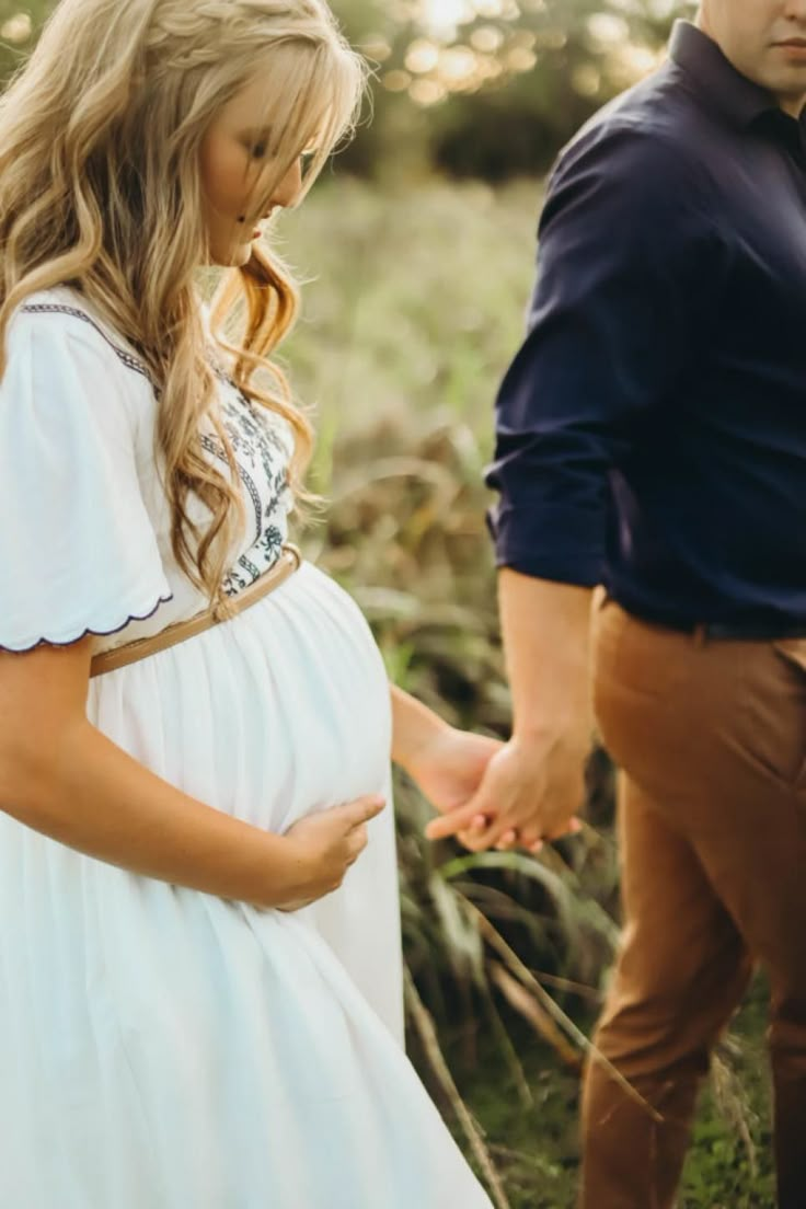 a pregnant woman in a white dress standing next to a man wearing a blue shirt