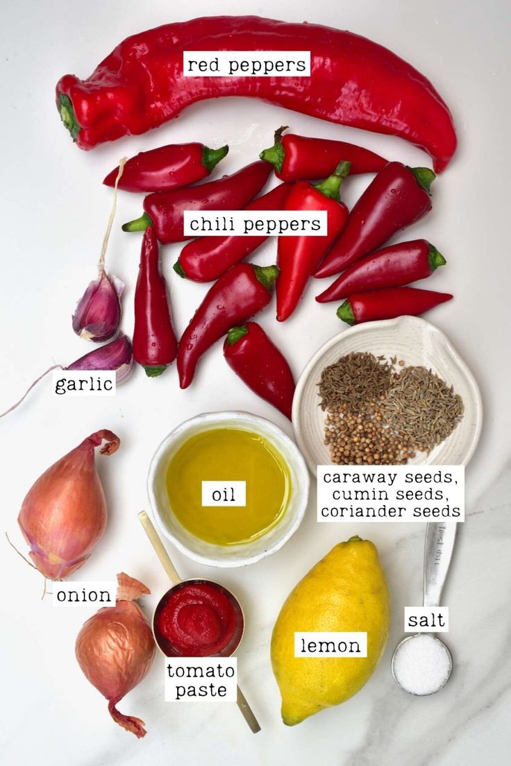 the ingredients for chili seasoning laid out on a white counter top, including peppers, lemons, garlic, salt and pepper