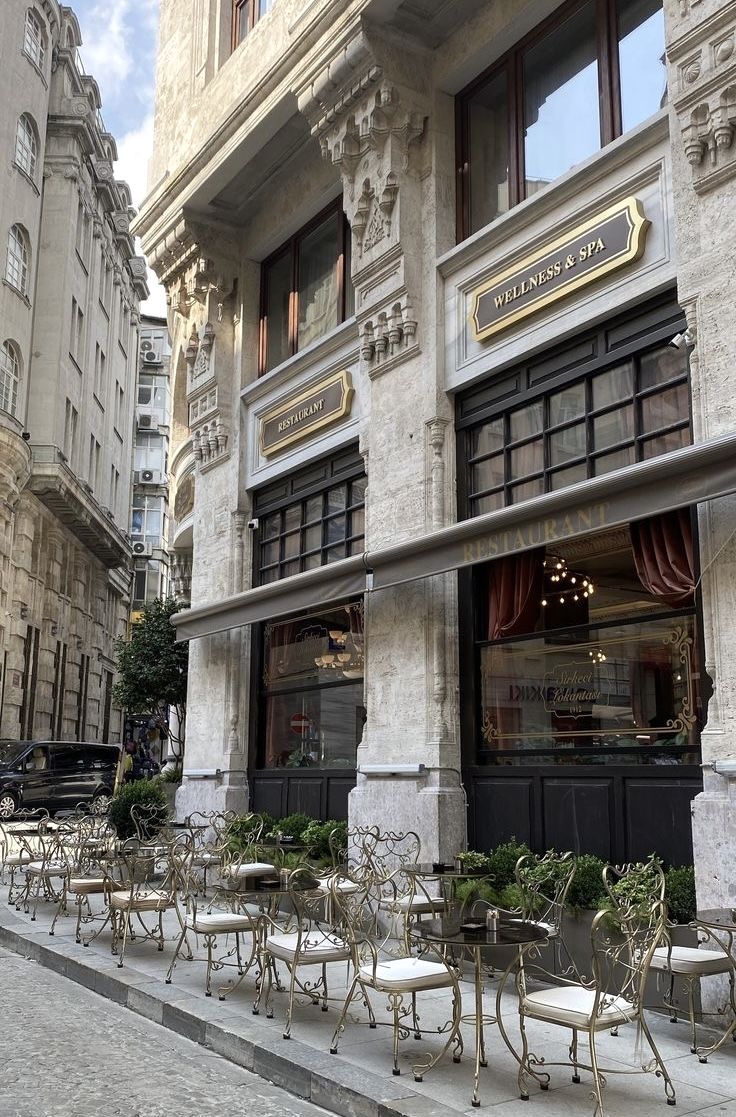 there are many tables and chairs on the sidewalk in front of this building with windows