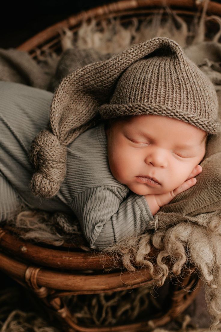 a baby sleeping in a basket wearing a hat