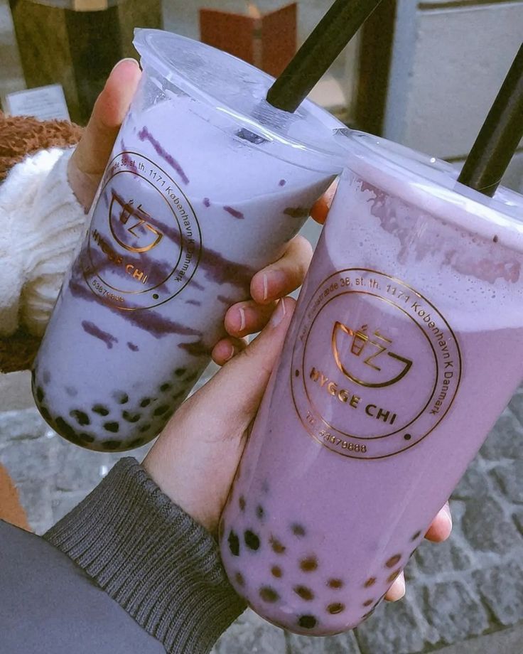 two people holding up drinks with straws in their hands, one is blue and the other has purple sprinkles on it