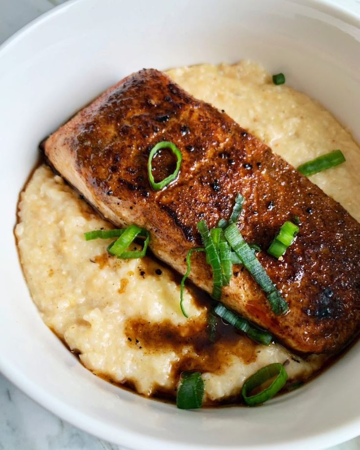 a white bowl filled with meat and mashed potatoes on top of a marble table