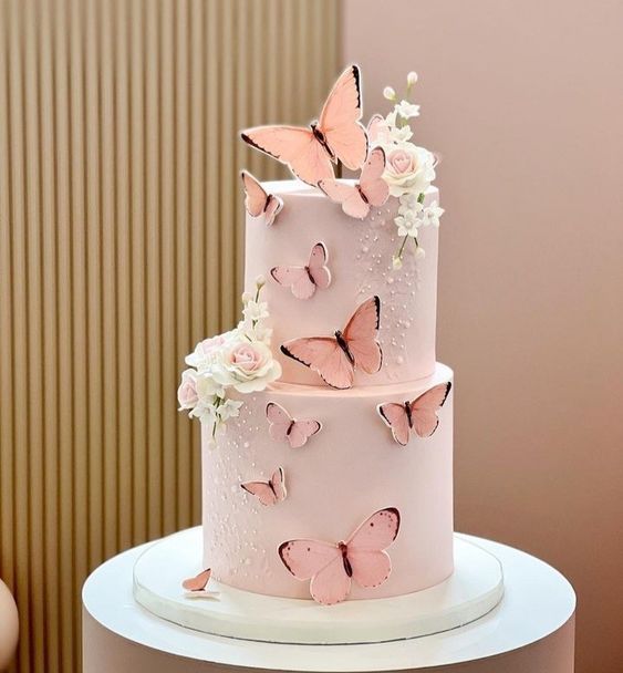 a three tiered cake with pink frosting and butterflies on the top is decorated with white flowers