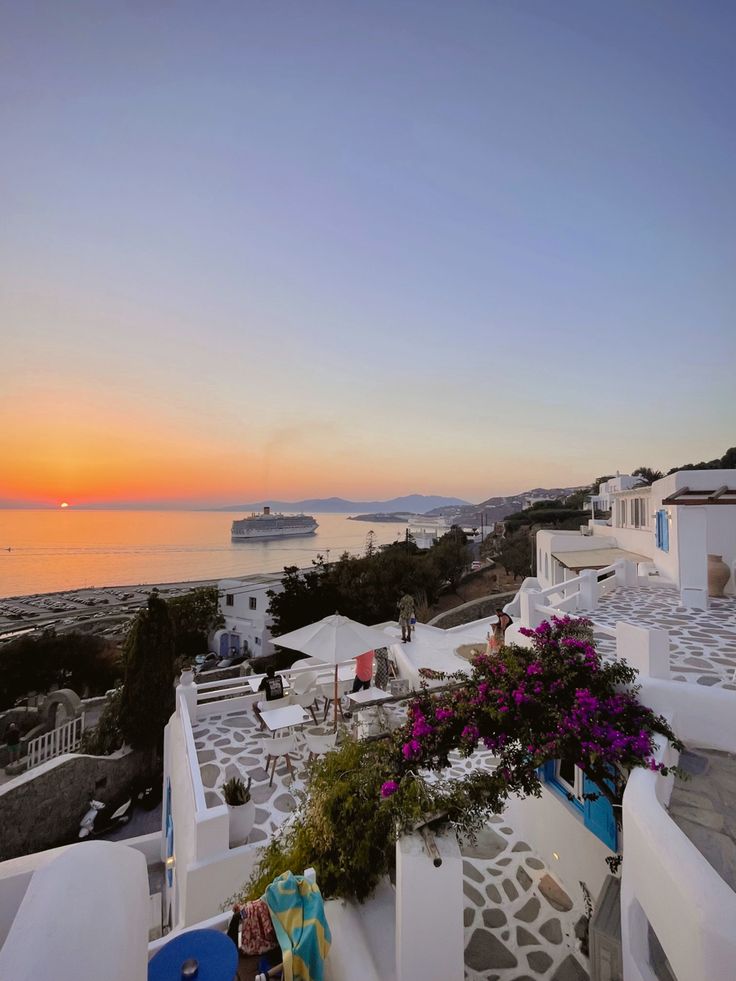 the sun is setting over some white buildings with flowers in front of it and a cruise ship in the background