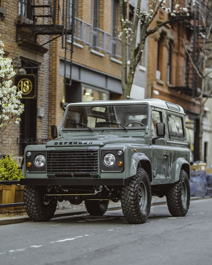 a green land rover is parked on the street in front of some brick buildings and trees