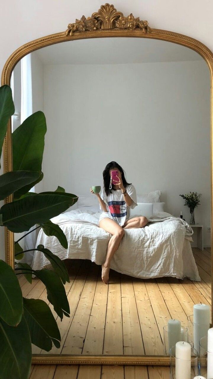 a woman sitting on top of a bed in front of a large gold framed mirror