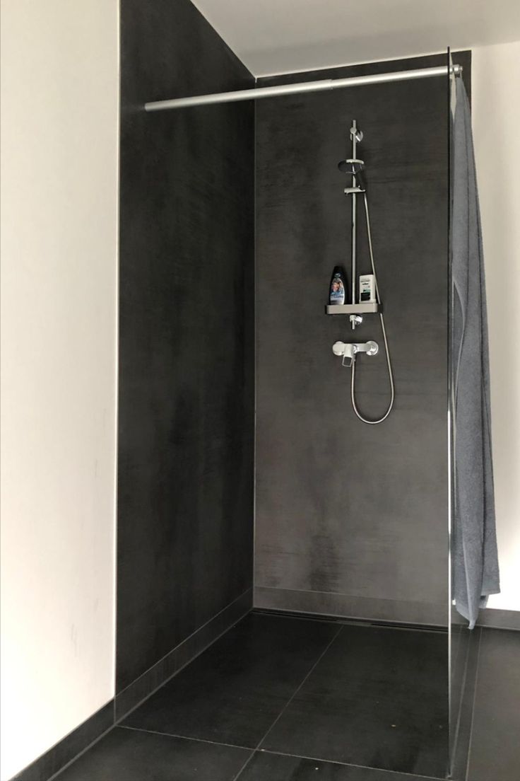 a bathroom with a walk in shower next to a white wall and black tile floor