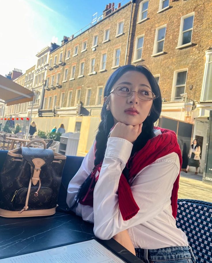 a woman sitting at an outdoor table with her hand on her chin and looking off into the distance