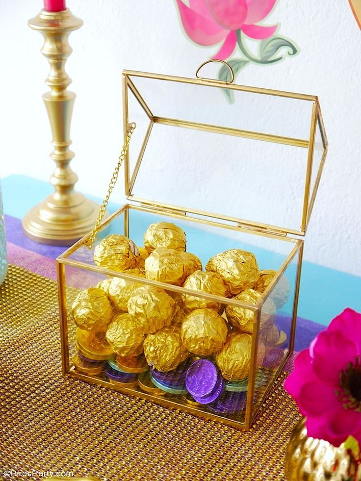 a glass box filled with chocolates on top of a table next to a pink flower