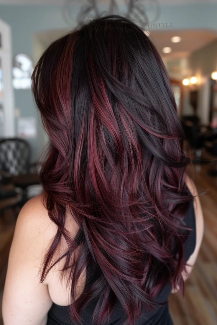 Woman with long, wavy brown hair with red highlights in a hair salon. Medium Brown Purple Hair, Cherry Red Hair Highlights On Black Hair, Deep Cherry Red Balayage, Dark Roots With Red Ends, Light Brown Hair Burgundy Highlights, Cherry Red Hair Styles, Red Thick Highlights, Light Red Highlights On Dark Hair, Brunette Hair With Burgundy Highlights