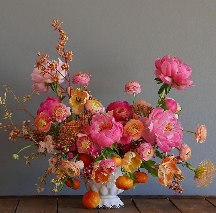 a white vase filled with lots of pink and orange flowers on top of a wooden table