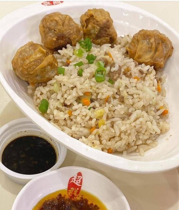 a white bowl filled with rice and meat next to two small bowls of dipping sauce